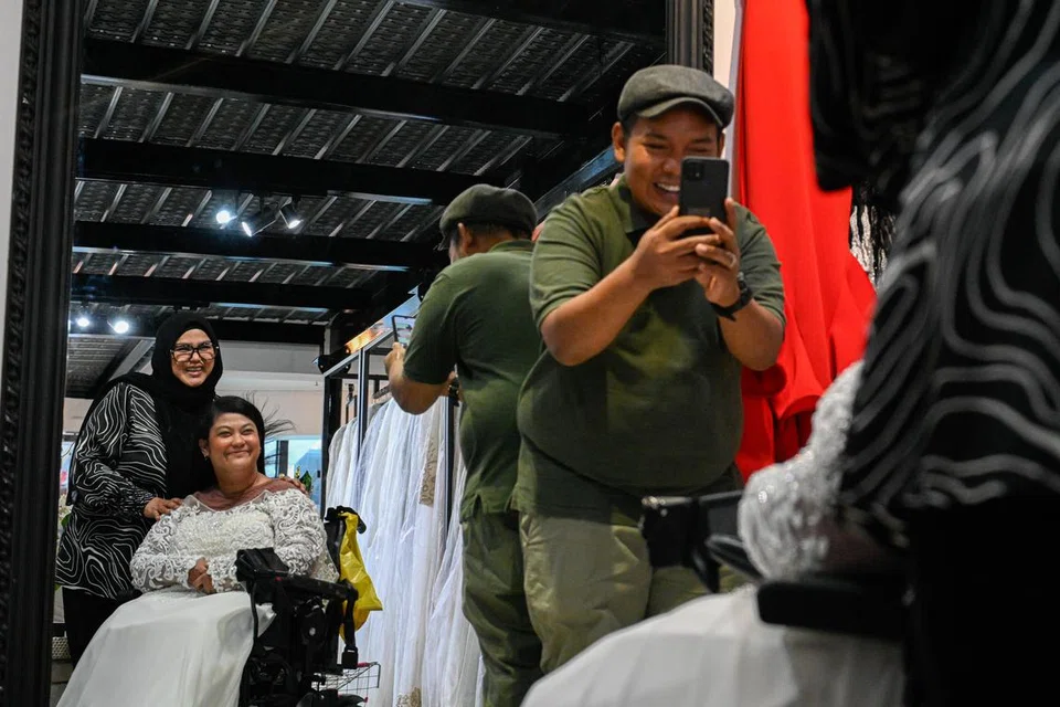 Cik Roszana Ali, yang menghidap palsi serebrum (duduk), mencuba pakaian pengantin di butik Fatimah Mohsin, The Wedding Gallery, dengan tunangnya Encik Herman mengambil gambarnya. Bersama dalam gambar ialah pemilik butik, Cik Fatimah.