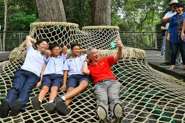 NIKMATI SUASANA DI ATAS POKOK: Encik Lee merakamkan gambar sambil bersantai bersama (dari kiri) Menteri Pembangunan Negara Lawrence Wong dan dua pelajar Sekolah Menengah Tanglin, Casey Lim dan Muhammad Nabil Ali. Mereka berbaring santai di atas Canopy Web di SPH Walk of Giants, antara tarikan utama Learning Forest. - Foto THE STRAITS TIMES