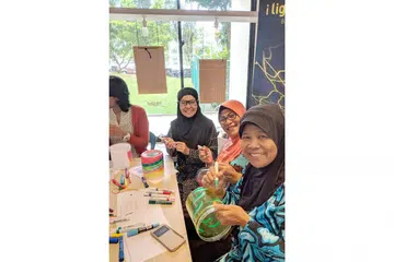 SUMBANG IDEA KREATIF: Cik Noriyah (bertudung jingga) bersama rakannya, Cik Sarimah Soeradi (berkaca mata) dan Cik Saharidah Suradi (berbaju biru), melukis bekas biskut PET mereka di bengkel prapesta di Jurong East bagi pemasangan seni lampu 'The Rainbow Connection'. - Foto BH oleh ZULAIQAH ABDUL RAHIM