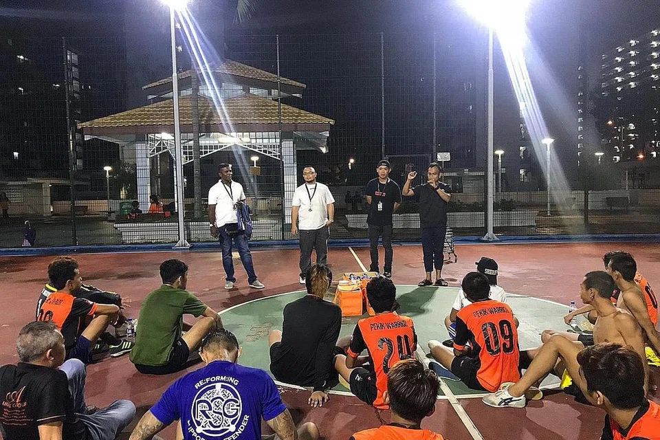 GABUNG TENAGA DEKATI BELIA: Encik Iqbal, pengasas Revive.sg (menghadap kamera, dua dari kiri), dan Encik Noor Halis, pengasas bersama One Heart Brothers Society (menghadap kamera, kanan), turun padang dalam acara futsal melibatkan remaja dan belia di estet perumahan Jalan Kukoh pada 11 November lalu. - Foto REVIVE.SG