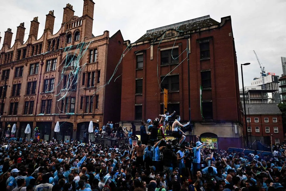 DISAMBUT DENGAN SORAKAN: Penyokong Manchester City bersorak sekehendak untuk menyambut ketibaan pemain pasukan kegemaran mereka. Pemain Manchester City dibawa berarak di sekeliling kota Manchester bagi meraikan pencapaian mereka memenangi tiga piala utama pada musim yang baru berakhir.