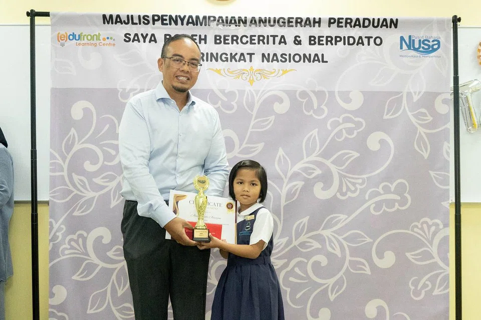JOHAN CILIK: (Gambar atas) Aleeya Aeiziyan daripada Sekolah Rendah Raffles Girls menjuarai pertandingan bercerita Kategori A untuk murid darjah 1 dan 2. Dia menerima anugerah daripada Pengarah Urusan Edufront Learning Centre, Encik Yang Iskandar Suratty. - Foto PUSAT BAHASA NUSA