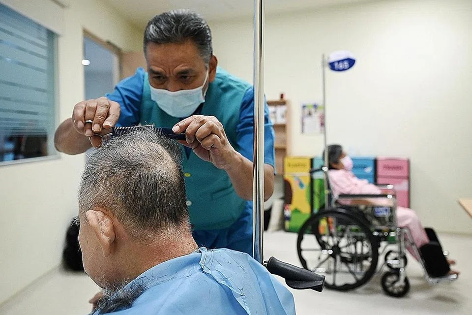 GUNTING RAMBUT: Sebulan sekali, Encik Taha meluangkan masa di Hospital Masyarakat Jurong untuk menggunting rambut pesakit yang tinggal di sana untuk jangka masa panjang. (Gambar atas) menunjukkan Encik Taha sedang menggunting rambut seorang pesakit. - Foto-foto BH oleh MOHD KHALID BABA