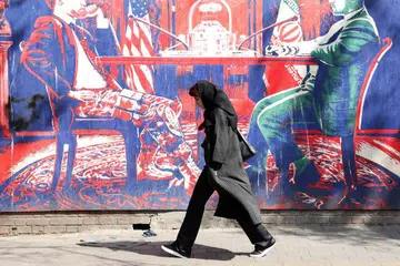 Seorang wanita Iran berjalan melepasi mural anti-Amerika yang menggambarkan rundingan antara Amerika Syarikat dengan Iran berhampiran bekas kedutaan Amerika Syarikat di Teheran, Iran.