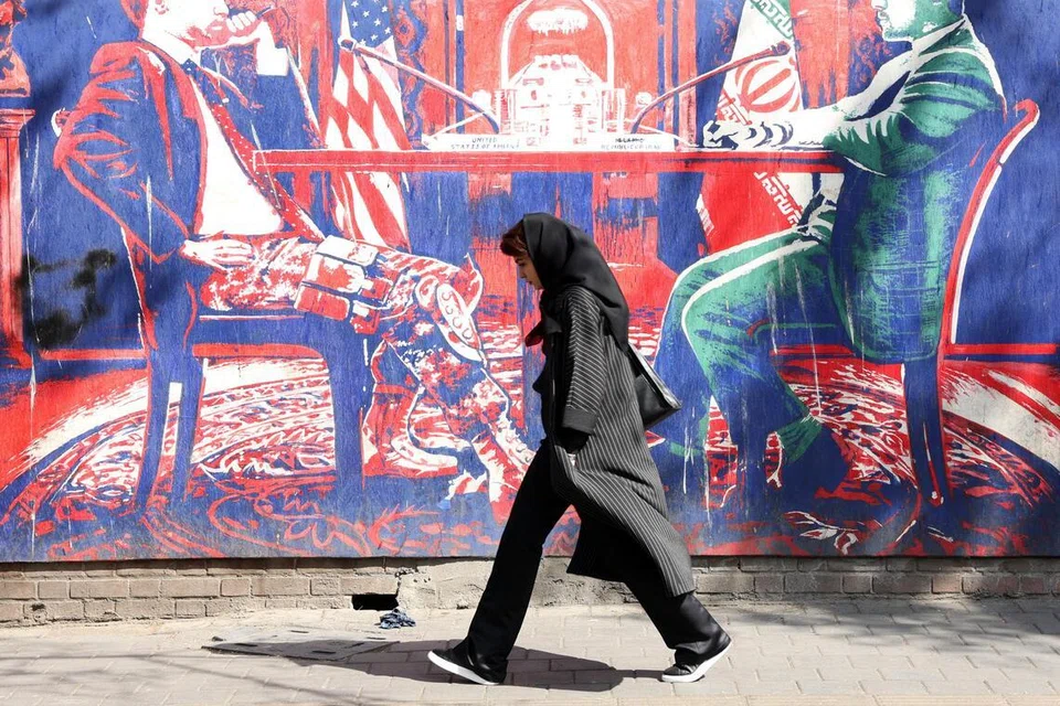 Seorang wanita Iran berjalan melepasi mural anti-Amerika yang menggambarkan rundingan antara Amerika Syarikat dengan Iran berhampiran bekas kedutaan Amerika Syarikat di Teheran, Iran.