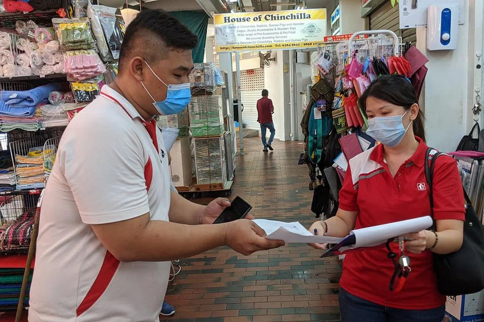WAJIB PAKAI PELITUP: Pengurus hartanah komersial di Lembaga Perumahan dan Pembangunan (HDB), Cik Jamie Neo (kanan), memberikan sokongan dengan menyumbang tenaga dalam rangkaian pegawai penguatkuasa semasa tempoh pemutus rantaian jangkitan ini. Beliau memberi nasihat kepada orang awam di Serangoon North untuk mematuhi langkah jarak selamat lebih ketat yang dilaksanakan. - Foto MASAGOS ZULKIFLI/FACEBOOK