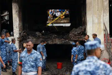 Orang ramai memerhati melalui tingkap yang pecah ketika anggota Tentera Udara Bangladesh menjalankan operasi di lokasi kejadian, selepas sebuah pesawat latihan tentera terhempas ke sebuah bangunan milik kampus Milestone School and College di Dhaka, Bangladesh, pada 22 Julai 2025. 