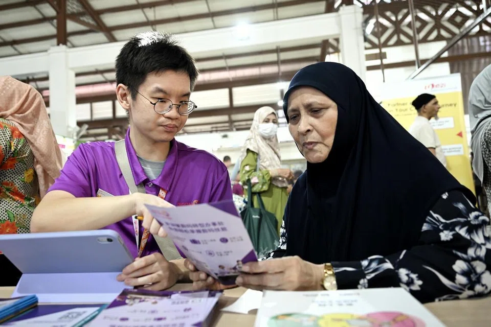 Cik Rokiah Abu Bakar (kanan), 70 tahun diperkenalkan kepada program-program meningkatkan keyakinan dan kemahiran terhadap AI oleh Duta Digital, Encik Timothy Lau Bi Wen (kiri), 31 tahun, semasa acara Pop-up AI Langkah Digital di Pasar Geylang Serai pada 22 Mei.