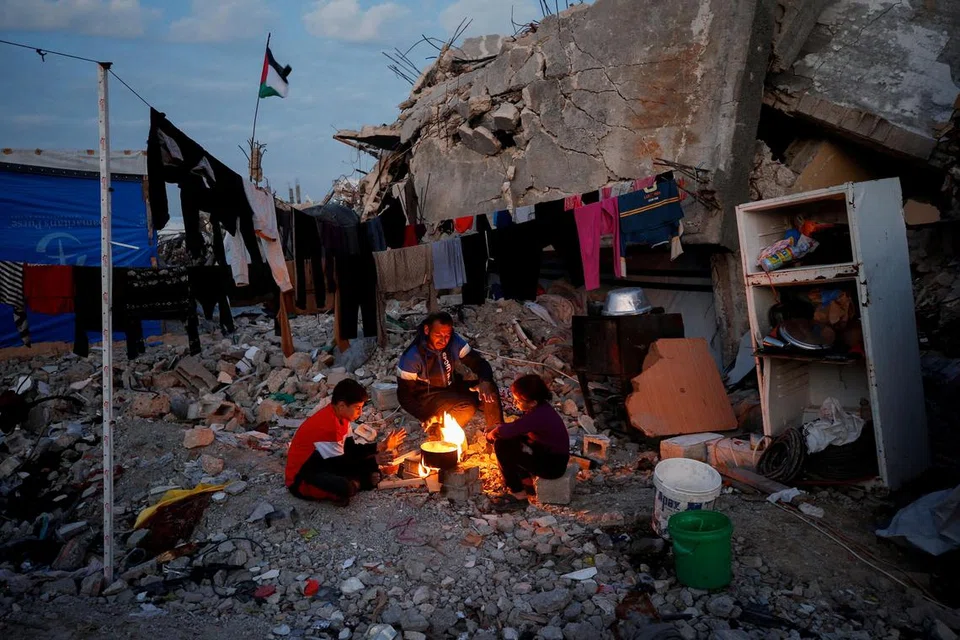 Sebuah keluarga Palestin duduk di sekeliling api di antara runtuhan bangunan yang musnah semasa serangan Israel, di tengah-tengah gencatan senjata antara Israel dan Hamas, di kem pelarian Jabalia, utara Semenanjung Gaza, pada 17 Februari. 