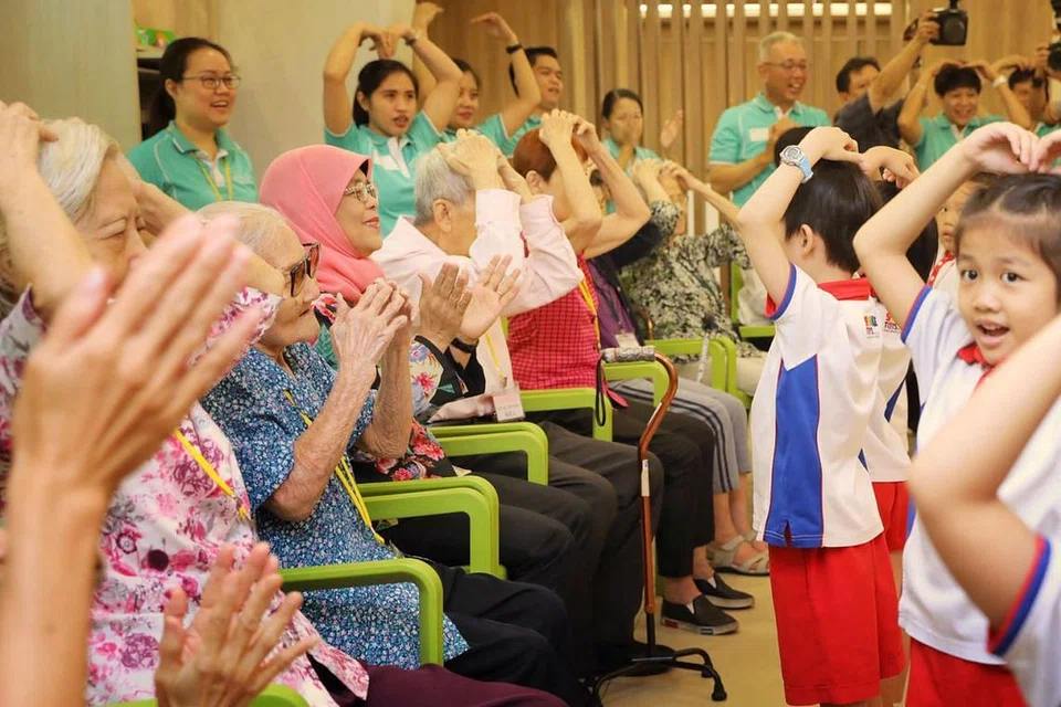 AKTIVITI SILANG GENERASI: Presiden Halimah (bertudung merah jambu) menyertai warga emas dan kanak-kanak melakukan aktiviti mingguan mereka di Sparkle Care @ Yew Tee yang merupakan kemudahan penjagaan warga emas bersepadu di bawah PCF. - Foto BH oleh GAVIN FOO