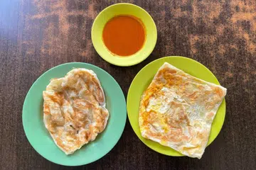 Roti perata kosong (kiri) dan roti perata telur (kanan) bersama kuah kari ikan yang masam dan pedas.