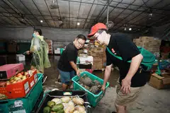 Pengasas bersama Food Rescue Sengkang (FRSK), Encik Derek Ong (seluar biru), mengangkat sebakul nanas yang diselamatkan daripada dibuang. 