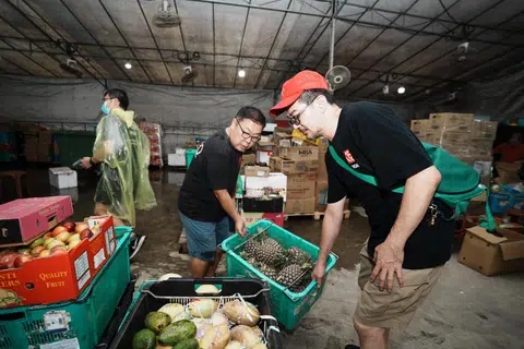 Pengasas bersama Food Rescue Sengkang (FRSK), Encik Derek Ong (seluar biru), mengangkat sebakul nanas yang diselamatkan daripada dibuang. 
