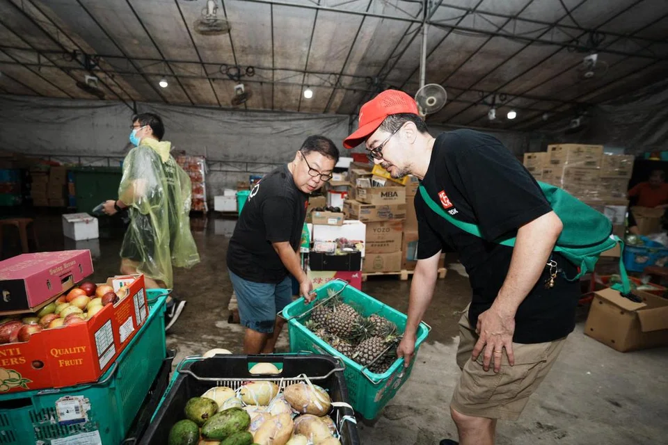 Pengasas bersama Food Rescue Sengkang (FRSK), Encik Derek Ong (seluar biru), mengangkat sebakul nanas yang diselamatkan daripada dibuang. 