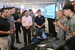 Menteri Negara Kanan (Pertahanan merangkap Kemampanan dan Sekitaran), Encik Zaqy Mohamad (kiri) bersama kakitangan Komand Pertahanan Siber di Ex SG Ready. Kakitangan itu, antara lain, menjalankan tugas risikan ancaman siber, forensik digital dan ujian penembusan siber. Menteri Penerangan dan Pembangunan Digital, Cik Josephine Teo (tiga dari kanan) turut mendengar taklimat ini.