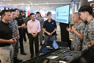 Menteri Negara Kanan (Pertahanan merangkap Kemampanan dan Sekitaran), Encik Zaqy Mohamad (kiri) bersama kakitangan Komand Pertahanan Siber di Ex SG Ready. Kakitangan itu, antara lain, menjalankan tugas risikan ancaman siber, forensik digital dan ujian penembusan siber. Menteri Penerangan dan Pembangunan Digital, Cik Josephine Teo (tiga dari kanan) turut mendengar taklimat ini.