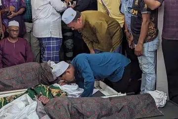 KUCUPAN TERAKHIR: Abdur Rahman Amir Ruddin (tunduk berbaju biru), anak sulung kepada pasangan Allahyarham Amir Ruddin Ismail, 46 tahun, dan Allahyarhamah Norahimah Noor Muhamad, 43 tahun mengucup buat kali terakhir jenazah ahli keluarganya yang maut dalam kemalangan di Kilometer 5, Jalan Segamat-Kuantan, Muar, Johor pada petang Jumaat.