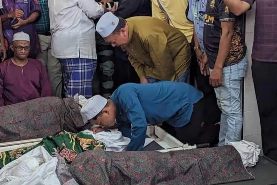 KUCUPAN TERAKHIR: Abdur Rahman Amir Ruddin (tunduk berbaju biru), anak sulung kepada pasangan Allahyarham Amir Ruddin Ismail, 46 tahun, dan Allahyarhamah Norahimah Noor Muhamad, 43 tahun mengucup buat kali terakhir jenazah ahli keluarganya yang maut dalam kemalangan di Kilometer 5, Jalan Segamat-Kuantan, Muar, Johor pada petang Jumaat.