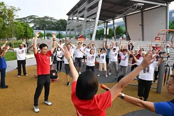 Menteri Kesihatan, Encik Ong Ye Kung (berbaju merah), melakukan senaman pemanasan badan bersama penduduk sebelum merasmikan permulaan acara Jalan @ Sembawang Central pada 12 April.