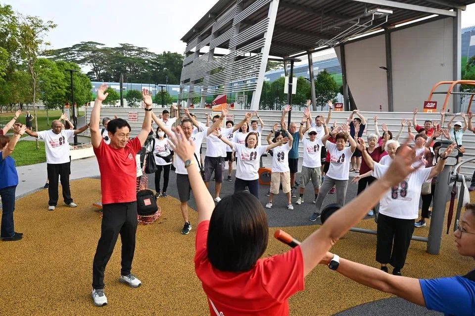 Menteri Kesihatan, Encik Ong Ye Kung (berbaju merah), melakukan senaman pemanasan badan bersama penduduk sebelum merasmikan permulaan acara Jalan @ Sembawang Central pada 12 April.