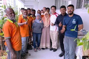 HULUR BANTUAN: Cik Maswati Masduki (empat dari kanan) bersama pekerja pembersihan kawasan Nee Soon, sukarelawan dan Encik Derrick Goh (berbaju putih) semasa sesi makan tengah hari sambutan Hari Raya di Blok 394, Yishun Clove.