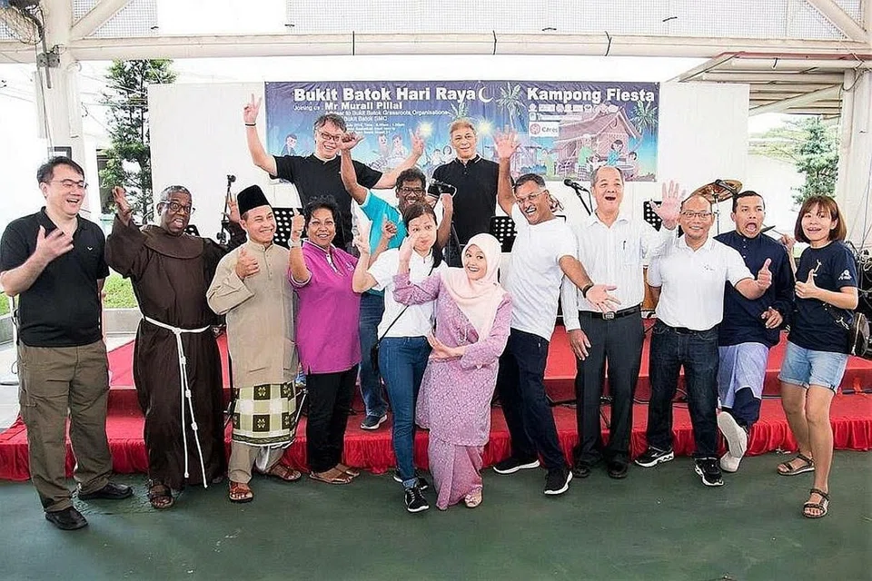 MERIAH BERSAMA: Relawan Gereja St Mary of Angels dan Masjid Ar-Raudhah bersama Anggota Parlimen (AP) GRC Jurong, Cik Rahayu Mahzam (bertudung), dan AP GRC Bukit Batok, Encik Murali Pillai (lima dari kanan), sama-sama menjayakan acara Bukit Batok Hari Raya-Kampong Fiesta yang mengagihkan makanan keperluan asas kepada keluarga yang memerlukan dan mengajak penduduk meraikan Hari Raya bersama. - Foto KELAB MASYARAKAT BUKIT BATOK