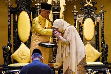 PENUH ISTIADAT ISTANA: Tunku Azizah Aminah Maimunah Iskandariah Sultan Iskandar, mencium tangan suaminya, Sultan Abdullah Ibni Sultan Ahmad Shah, semasa upacara pemasyhuran Sultan Pahang itu. - Foto AFP
