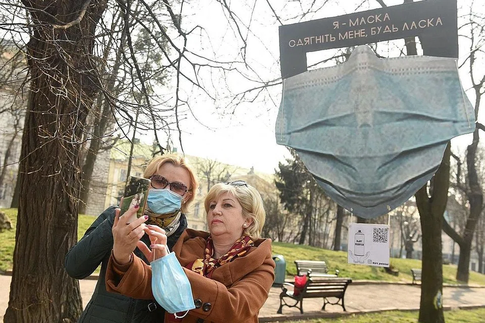 PELITUP 'GERGASI': Dua wanita ini mengambil gambar selfie di hadapan hiasan pelitup besar dengan kekata 'Saya pelitup, tolonglah pakai saya' di bandar Lviv di barat Ukraine. 