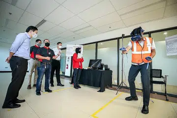TINJAU LATIHAN: Encik Lawrence Wong (kiri) memerhatikan peralatan latihan simulasi VR yang ditunjukkan oleh dua penolong pengurus stesen SMRT, Encik Zul Fadli (kanan) dan Cik Amira Natasya (berbaju merah). - Foto ZAOBAO