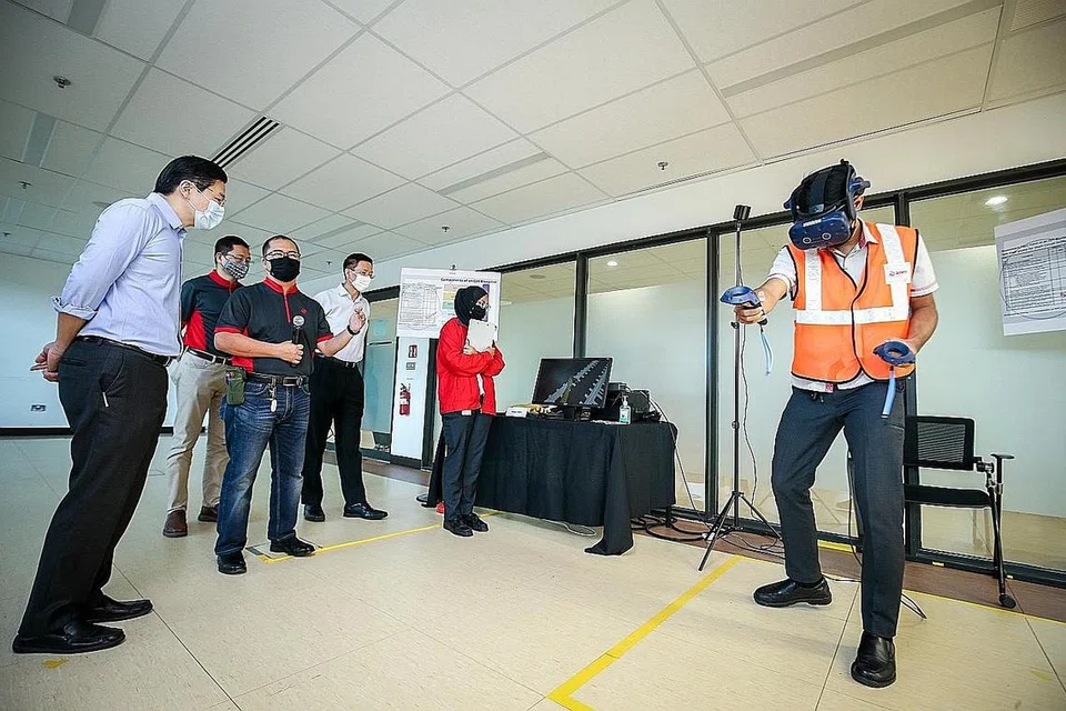 TINJAU LATIHAN: Encik Lawrence Wong (kiri) memerhatikan peralatan latihan simulasi VR yang ditunjukkan oleh dua penolong pengurus stesen SMRT, Encik Zul Fadli (kanan) dan Cik Amira Natasya (berbaju merah). - Foto ZAOBAO