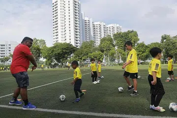 INGIN ISI JURANG: Jurulatih bola sepak Shahul Hamid (baru merah) melatih sekumpulan budak-budak lelaki, termasuk seorang kanak-kanak autistik, dalam gambar yang dirakam pada 10 April 2021 ini. Beliau menubuhkan program HotShotz yang menawarkan program latihan bola sepak hujung minggu di Sekolah Victoria. - Foto BH oleh ALPHONSUS CHERN 