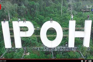 Lapan anak muda, termasuk tiga wanita, memasang buaian pada tanda gergasi 'IPOH' dan mengambil gambar menggunakan dron. Mereka kelihatan tidak memakai alat keselamatan. 