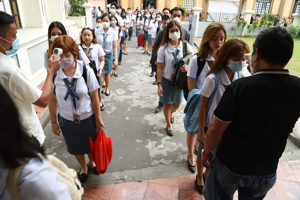 PEMERIKSAAN SUHU: Kakitangan mengambil suhu pelajar sebelum mereka memasuki kampus sebuah kolej di Manila. - Foto AFP