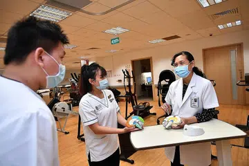 TUNJUK AJAR: Cik Suhana Salim (kanan) berkongsi ilmu dengan pelajar tahun keempat Institut Teknologi Singapura (SIT) Encik Ivan Tan Yong Tsu dan Cik Tan Yan Ni, di klinik Fisioterapi di Hospital Tan Tock Seng. - Foto BH oleh LIM YAOHUI