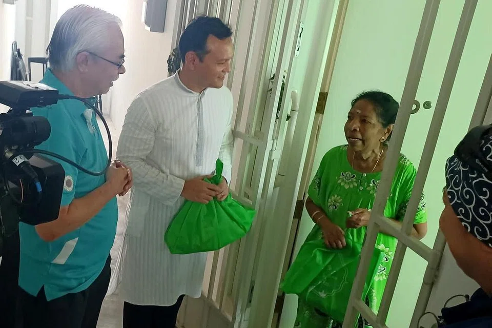 MENYEBAR KECERIAAN: (Dari kiri) Encik Ramamoorthy dan Encik Zaqy mengagihkan habuan kepada salah seorang penduduk di Blk 185A Woodlands Street 13 semalam sempena perayaan Deepavali. - Foto ihsan NARPANI PEARAVAI