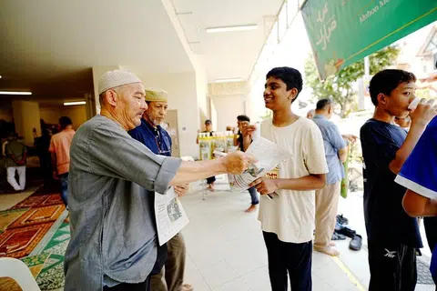 Pekerja di Masjid Khalid, Encik Hanafi Mohd Sidek (kiri), memberi naskhah BH kepada jemaah, termasuk pelajar Sekolah Menengah Broadrick, Mohamed Sahil Mohamed Sahbir (kanan).
