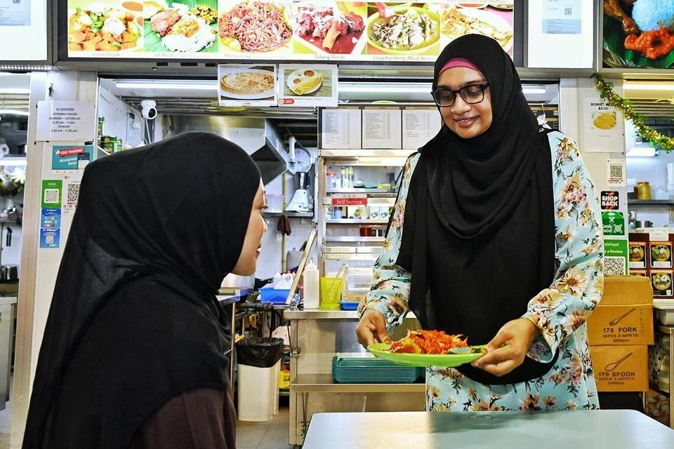 Penjaja, Cik Noor Aisha Mohamed Ibrahim (kanan), menjual makanan India Muslim di Pusat Penjaja Perusahaan Sosial di Pusat Penjaja Jurong West selepas pernah berniaga di sebuah kedai kopi dan medan selera. 