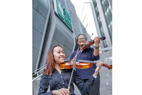 MUZIK KLASIK DEKAT DI HATI: Cik Nur Raeesah Abdul Malik (kiri) dan Cik Humaira Jasni menganggotai Kelab Ensembel Alat Tali Institusi Pengurusan Singapura (SIM) kerana ingin menggilap seberapa banyak ilmu menggesek biola dan membuat persembahan di khalayak ramai. Saksikan mereka beraksi dalam konsert klasik 'SIMphony 9 - Viaggio' di Teater Seni Pementasan SIM Sabtu ini. - Foto SIM