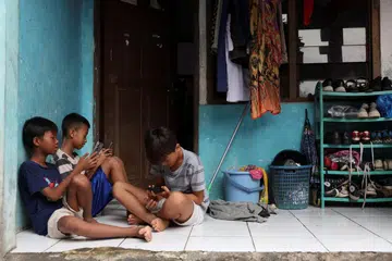 Affan Haritsah, 11 tahun, Daffa Ibnu Alkhalifi, 12 tahun, dan Kevin Prince, 14 tahun, menggunakan telefon bimbit mereka ketika Kementerian Komunikasi dan Digital Indonesia melaksanakan sekatan terhadap platform media sosial yang dikategorikan “berisiko tinggi” termasuk Facebook, TikTok dan Roblox di Depok, pinggir Jakarta, Indonesia pada 28 Mac 2026.
