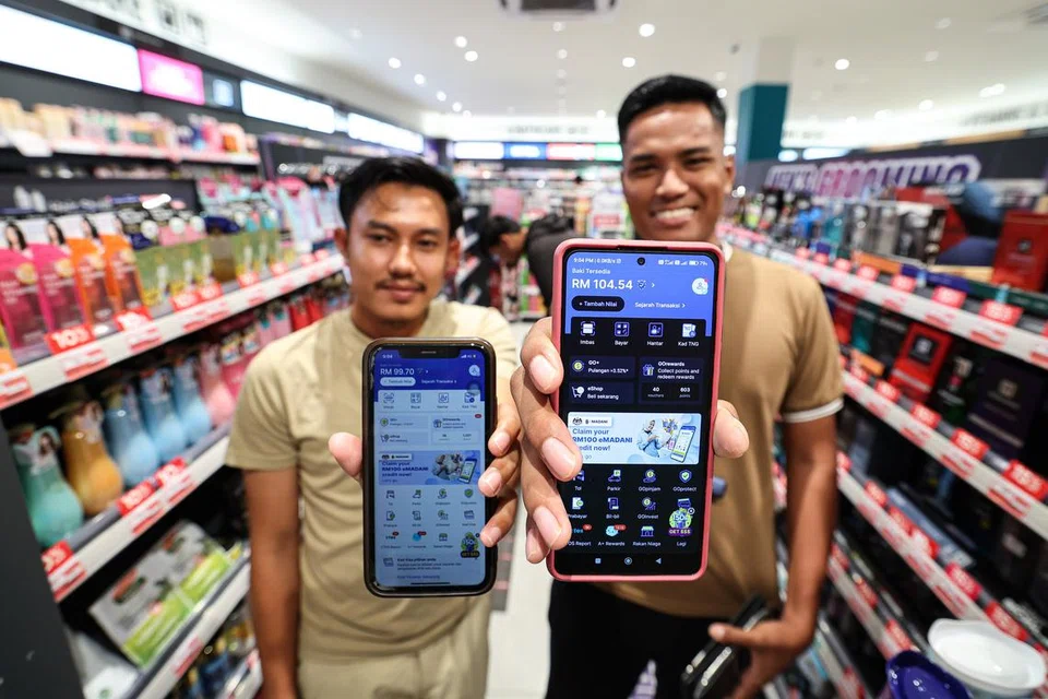 MULA BERBELANJA: Penerima kredit e-dompet, e-Madani sebanyak RM100, Encik Alif Ashraf Abdul Halim, 23 tahun, (kiri) dan Encik Mohd Asri Abdullah, 26 tahun (kanan), menunjukkan aplikasi Touch n Go E-wallet ketika melakukan pembelian secara kod tanpa sentuh (QRPAY) di premis yang menerima pembayaran tanpa tunai di  Ipoh pada malam 5 Disember.