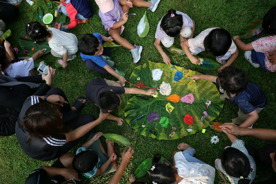 Kanak-kanak dan ibu bapa mereka melukis di atas daun besar dan menghiasinya menggunakan bunga dikumpul mereka semasa meneroka di luar.
