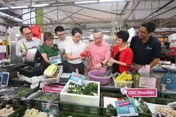 SKIM BANTUAN: Timbalan Perdana Menteri merangkap Menteri Perdagangan dan Perusahaan, Encik Gan Kim Yong (tiga dari kanan), bersama (dari kiri) Timbalan Pengerusi CDC North West, Encik Liang Eng Hwa; Mayor CDC Central, Cik Denise Phua Lay Peng; Mayor CDC North East, Encik Baey Yam Keng; Pengurus Besar Ai Muay Group, Encik Joe Chen Kangwei; Pengerusi Jawatankuasa Mayor yang juga Mayor CDC South West, Cik Low Yen Ling; dan Mayor CDC South East, Encik Dinesh Vasu Dash, meninjau sayur-sayuran yang dijual di Blok 168, Punggol Field Road, pada 2 Januari, menyusuli pelancaran baucar CDC.