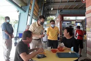 GIAT BERKEMPEN: Encik Andy Zhu (berdiri, baju kuning), Pengerusi Parti Pembaharuan, dan anggota parti, Cik Tyeisha Syaquilla (dua dari kanan) giat berkempen di pusat makanan Cheng San semalam. - Foto BH oleh ALPHONSUS CHERN