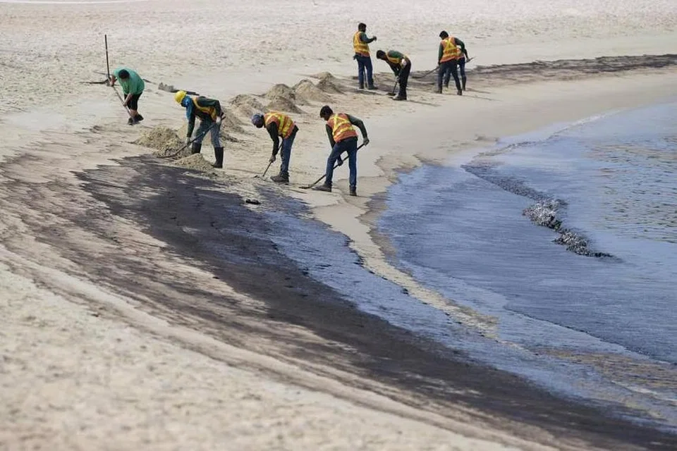 Sekumpulan pekerja membersihkan tumpahan minyak yang dikesan di perairan pantai Tanjong di Sentosa pada 15 Jun.