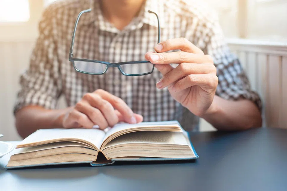 The young man with vision problems is picking up his glasses and reading a book.