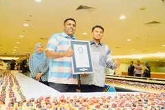 Pengerusi Jawatankuasa Perpaduan, Budaya dan Warisan Johor, Encik K. Raven Kumar (kiri), bersama Pengarah Tourism Johor, Encik Mohammad Nazrul Abd Rahim (kanan), menunjukkan sijil Rekod Dunia Guinness bagi rekod barisan tart terpanjang.
