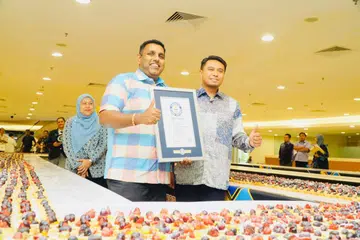 Pengerusi Jawatankuasa Perpaduan, Budaya dan Warisan Johor, Encik K. Raven Kumar (kiri), bersama Pengarah Tourism Johor, Encik Mohammad Nazrul Abd Rahim (kanan), menunjukkan sijil Rekod Dunia Guinness bagi rekod barisan tart terpanjang.