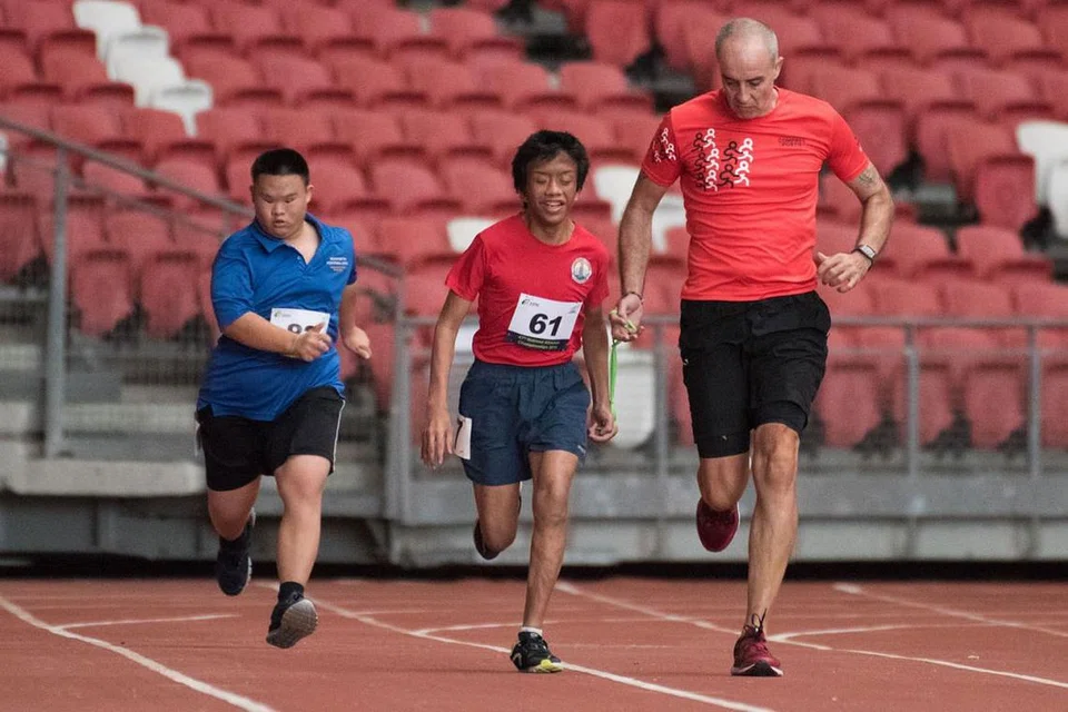 SEMANGAT BERKOBAR-KOBAR: Muhammad Sufian Abdullah (tengah) dari Sekolah Lighthouse mendapat bimbingan seorang pegawai semasa bersaing bagi acara 100 meter kategori T11-13. Di kiri ialah Jason Gan dari Sekolah Vokasional Mountbatten, yang tampil dalam kategori II2 yang diperkenalkan buat pertama kali. - Foto STEVEN HEE / SDSC 