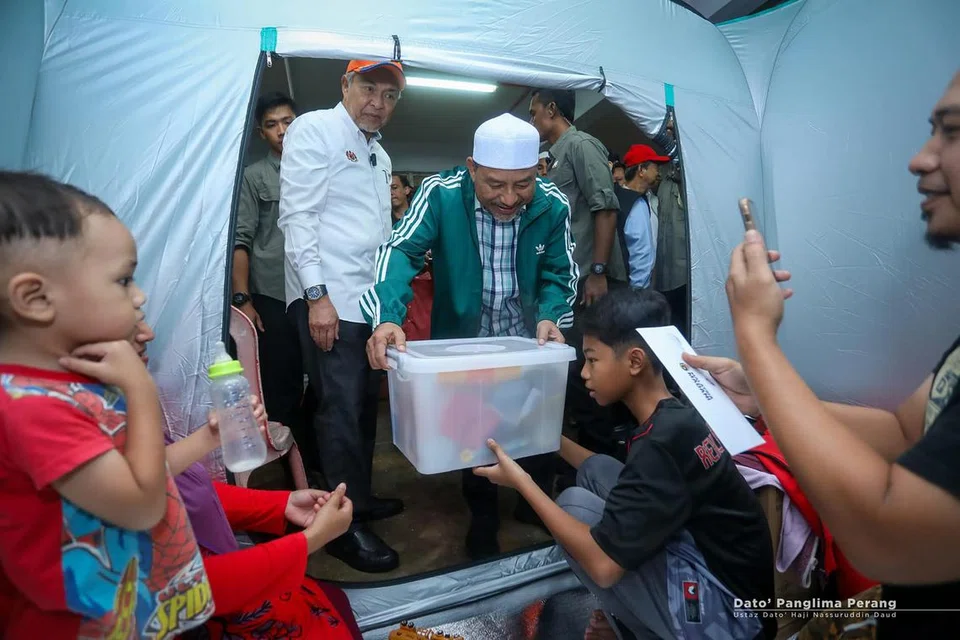 Timbalan Perdana Menteri, Datuk Seri Dr Ahmad Zahid Hamidi (berkemeja putih), bersama Menteri Besar Kelantan, Datuk Nassuruddin Daud (berjaket hijau), mengagihkan bantuan kepada mangsa banjir di sebuah pusat pemindahan sementara di Kota Bahru, Kelantan, pada 29 November.