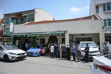 BERATUR PANJANG: Barisan panjang melimpah ke jalan dan kaki lima di luar kedai Indian Muslim Bakery & Confectionery Pte Ltd di Onan Road semalam, apabila pelanggan menanti untuk membeli karipap dan juadah lain sebelum kedai itu berhenti operasi pada Ahad.
